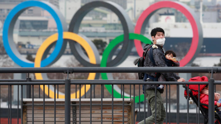 A person wears a face mask against Covid-19 on the Odaiba waterfront in Tokyo with Olympic rings in the background, on January 26, 2021.